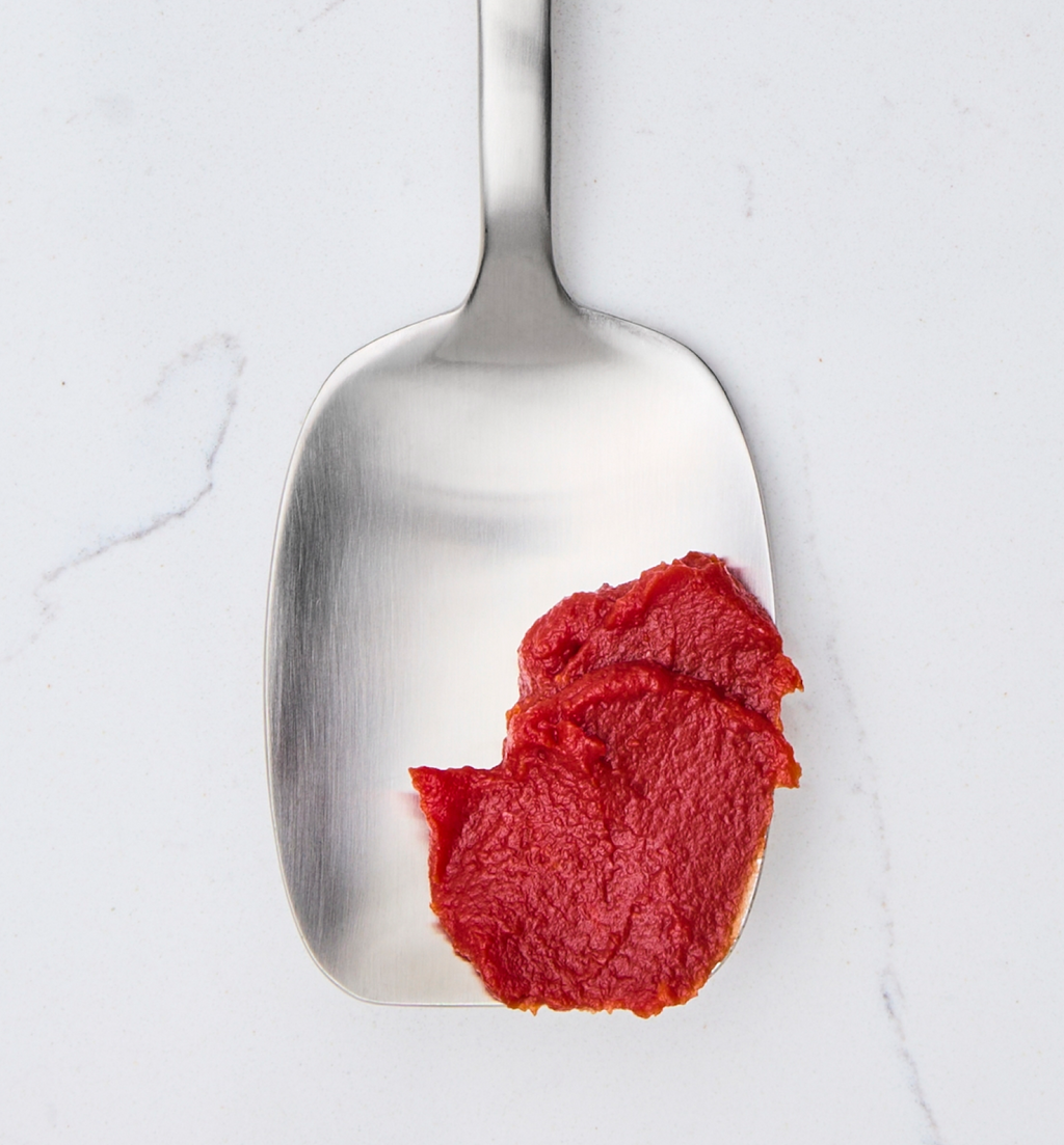 Tomato paste on a stainless steel spoon against marble background